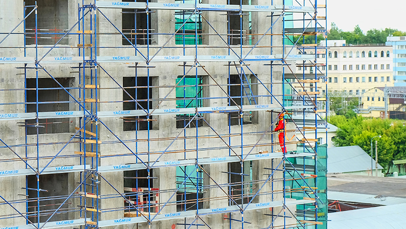 Laborer works on scaffolding on the facade of a growing residential building